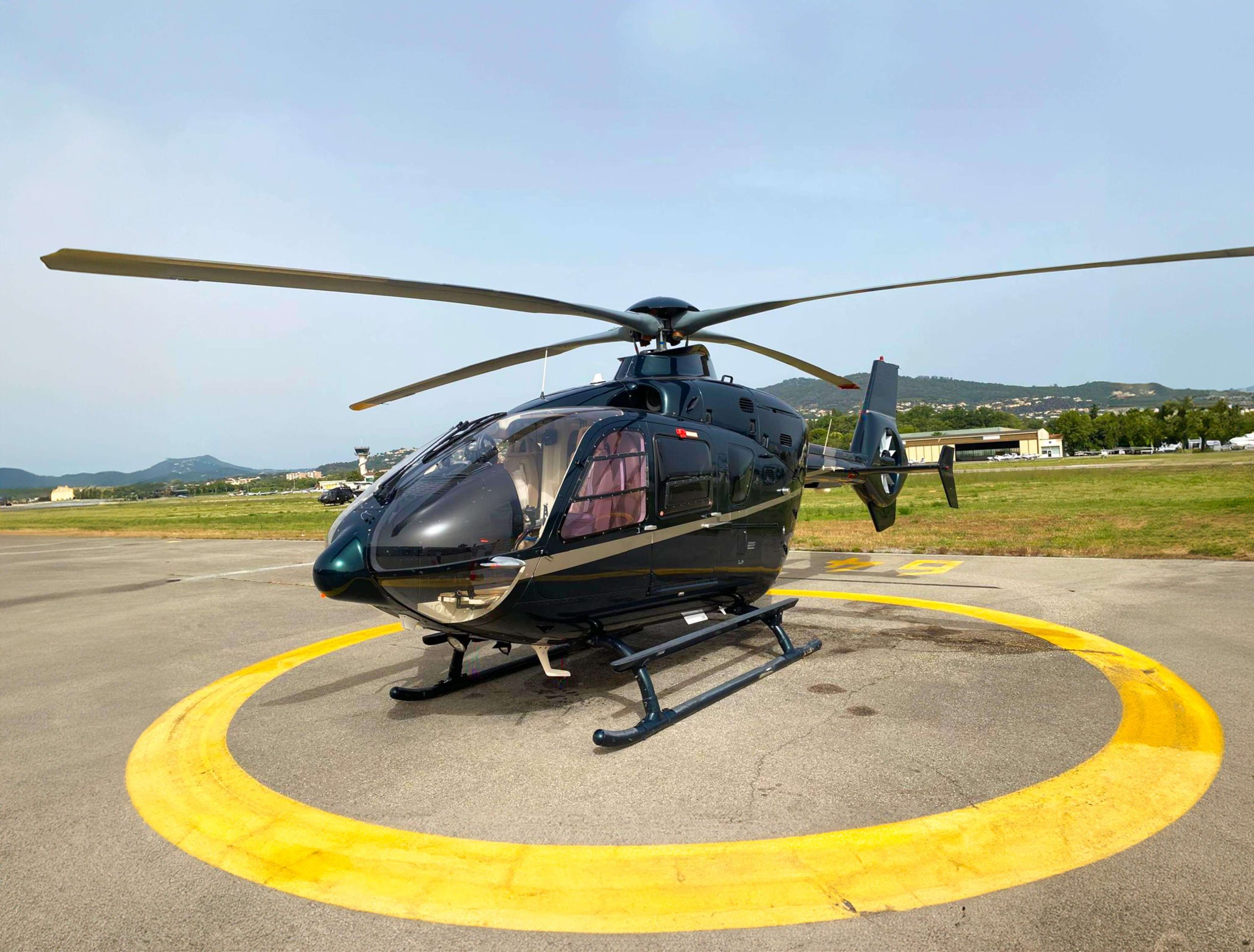 Hélicoptère noir stationné sur un héliport entouré de collines
